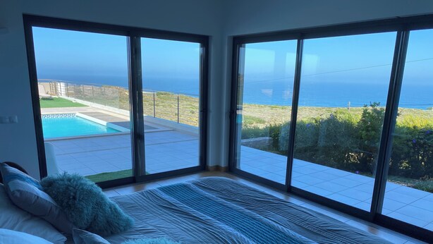 A bedroom with a large bed, two windows, and a view of a pool and ocean.
