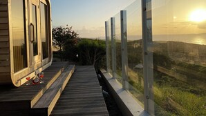 A wooden building with large glass doors and a wooden deck leading to a glass railing overlooking a coastal landscape.