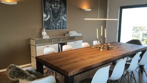 A modern dining area with a wooden table, white chairs, a Buddha statue, and a large framed artwork on the wall.