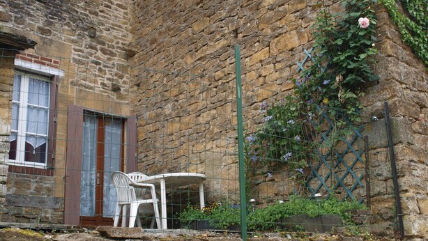 Un bâtiment en pierre avec une fenêtre et une porte, une chaise blanche et une table à l’extérieur.