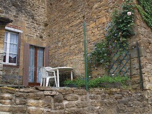 Un edificio de piedra con una ventana y una puerta, una silla blanca y una mesa afuera.