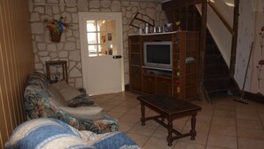 Un salon avec un mur en pierre, un canapé, un téléviseur posé sur un meuble en bois et un escalier.