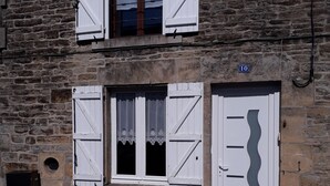 Un bâtiment en pierre avec des volets blancs, une plaque portant le numéro « 10 », et un pot de fleurs posé sur le sol.