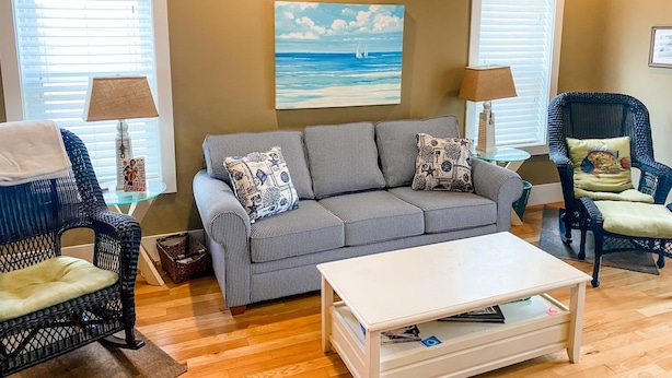 A living room with a striped sofa, two armchairs, a coffee table, and a painting of a beach scene.