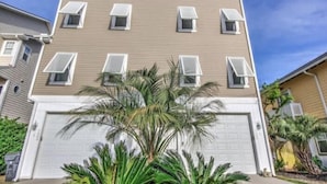 A multi-story residential building with a beige exterior, white garage doors, and multiple windows with awnings.