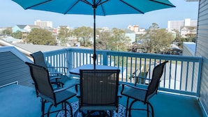 A balcony with a table and chairs, a blue umbrella, and a view of surrounding buildings.