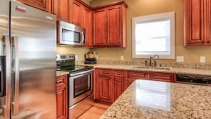 A kitchen with wooden cabinets, stainless steel appliances, granite countertops, and a window with blinds.