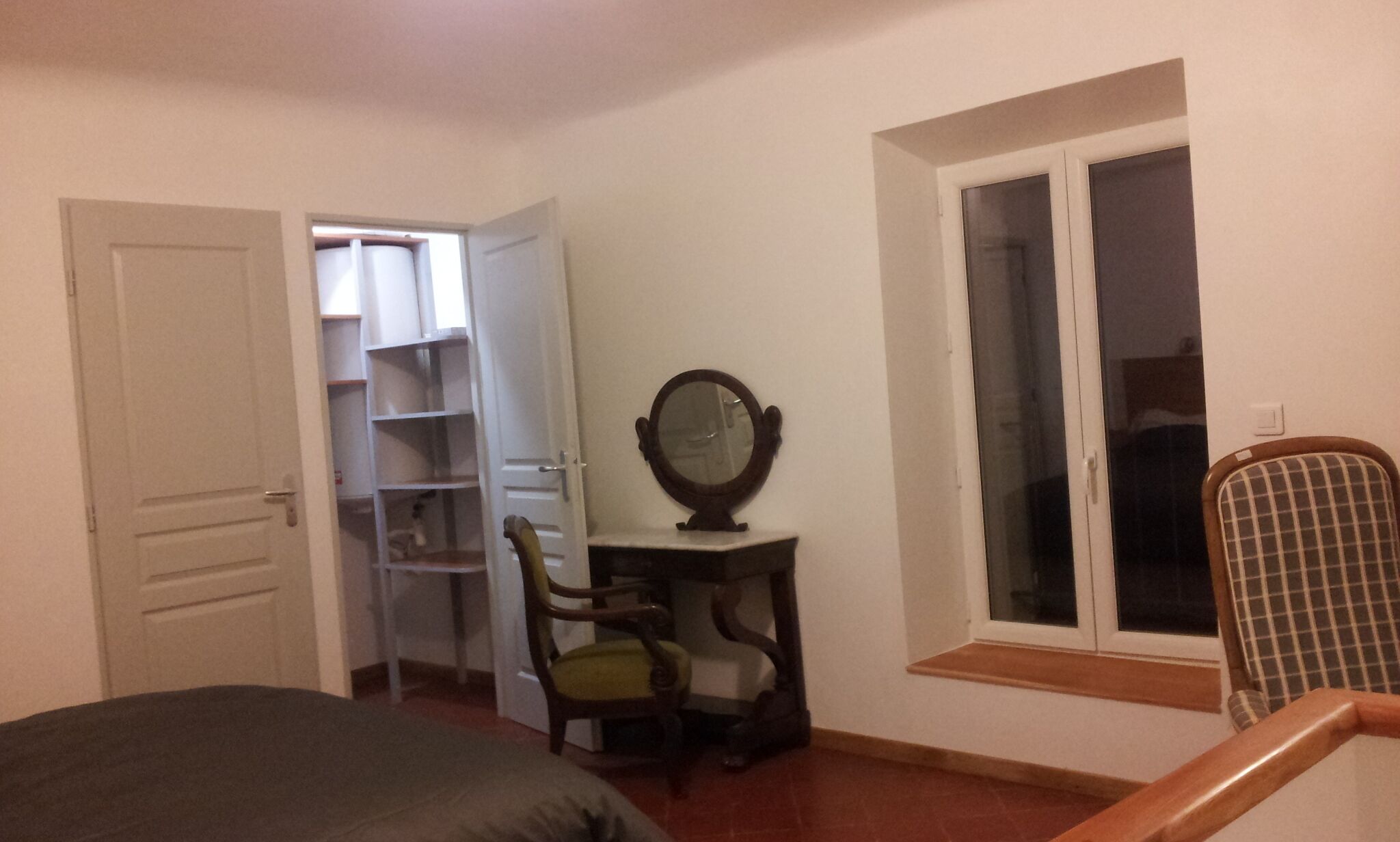 A bedroom with a bed, a chair, a desk with a mirror, a window, and a closet.