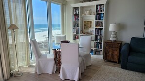 Un soggiorno con vista sulla spiaggia, una libreria, un tavolo da pranzo con sedie e un divano blu.