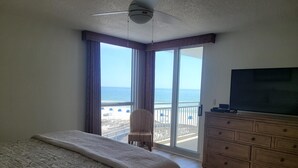 Una camera da letto con un letto grande, un comò, una televisione e un balcone vista spiaggia e mare.