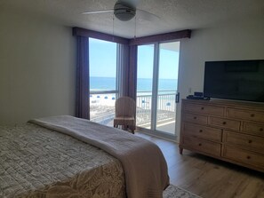 Une chambre dotée d’un grand lit, d’une commode, d’une télévision et d’un balcon offrant une vue sur la plage et l’océan.