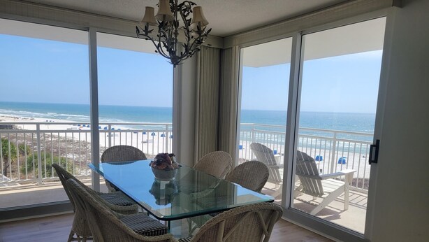 Un balcone con un tavolo in vetro e sedie in vimini, con vista su una spiaggia e una limpida visuale sull'oceano.