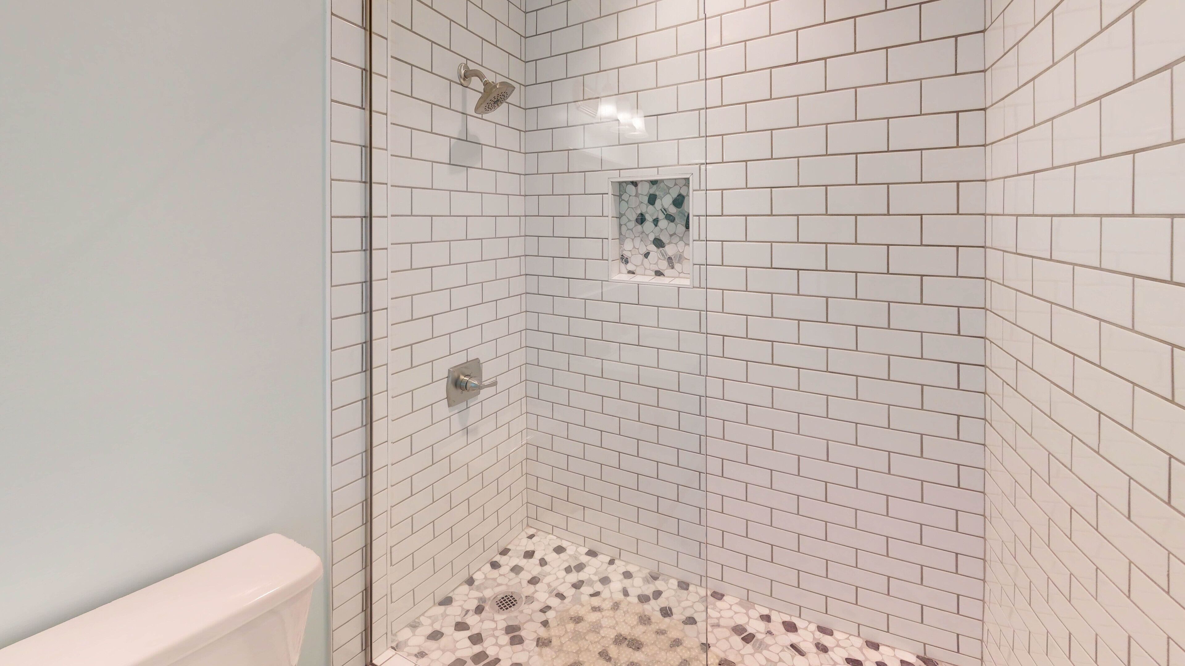 Ducha con azulejos blancos tipo metro y detalles en mosaico.