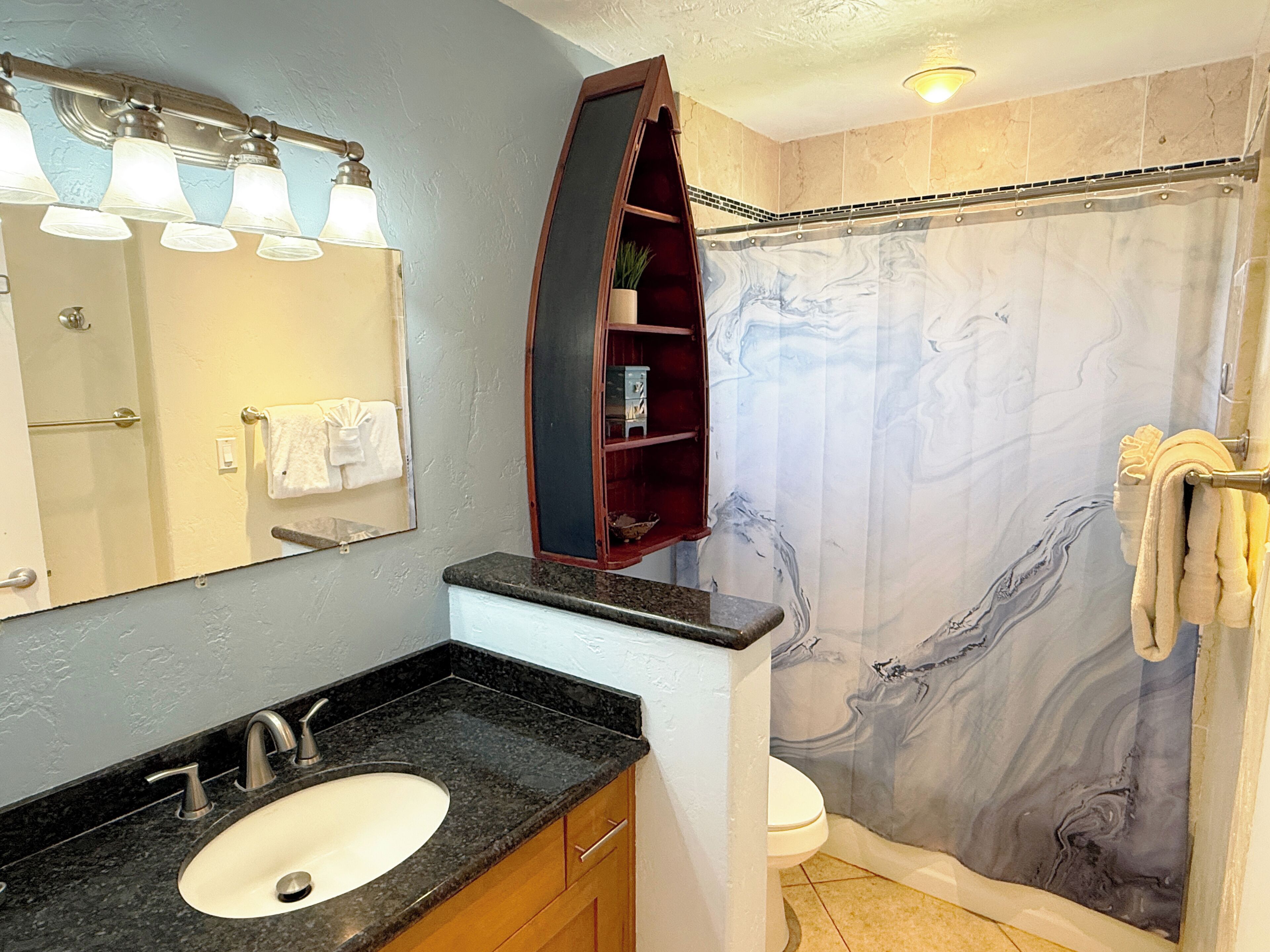 Une salle de bain avec un rideau de douche en marbre, un lavabo doté d’un plan de travail noir et un miroir au-dessus du lavabo.
