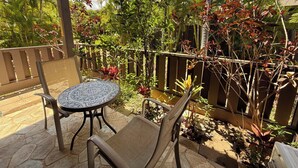 An outdoor patio with a round table and two chairs, surrounded by lush tropical plants and a wooden fence. - Where Zen Finds You Kihei Garden Condo Split AC Pool Hot Tub Near Beach (Kihei)