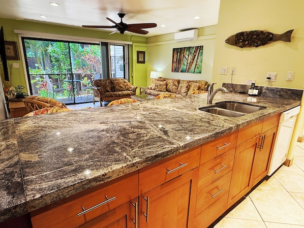A kitchen with granite countertops, wooden cabinets, a stainless steel sink, and a ceiling fan.