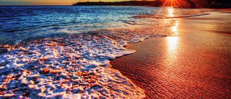 A beach with waves at sunset, a clear sky, and distant landforms.