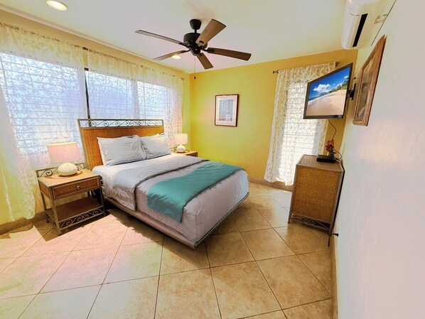 A bedroom with a bed, nightstands, a ceiling fan, a television, and a window with curtains.