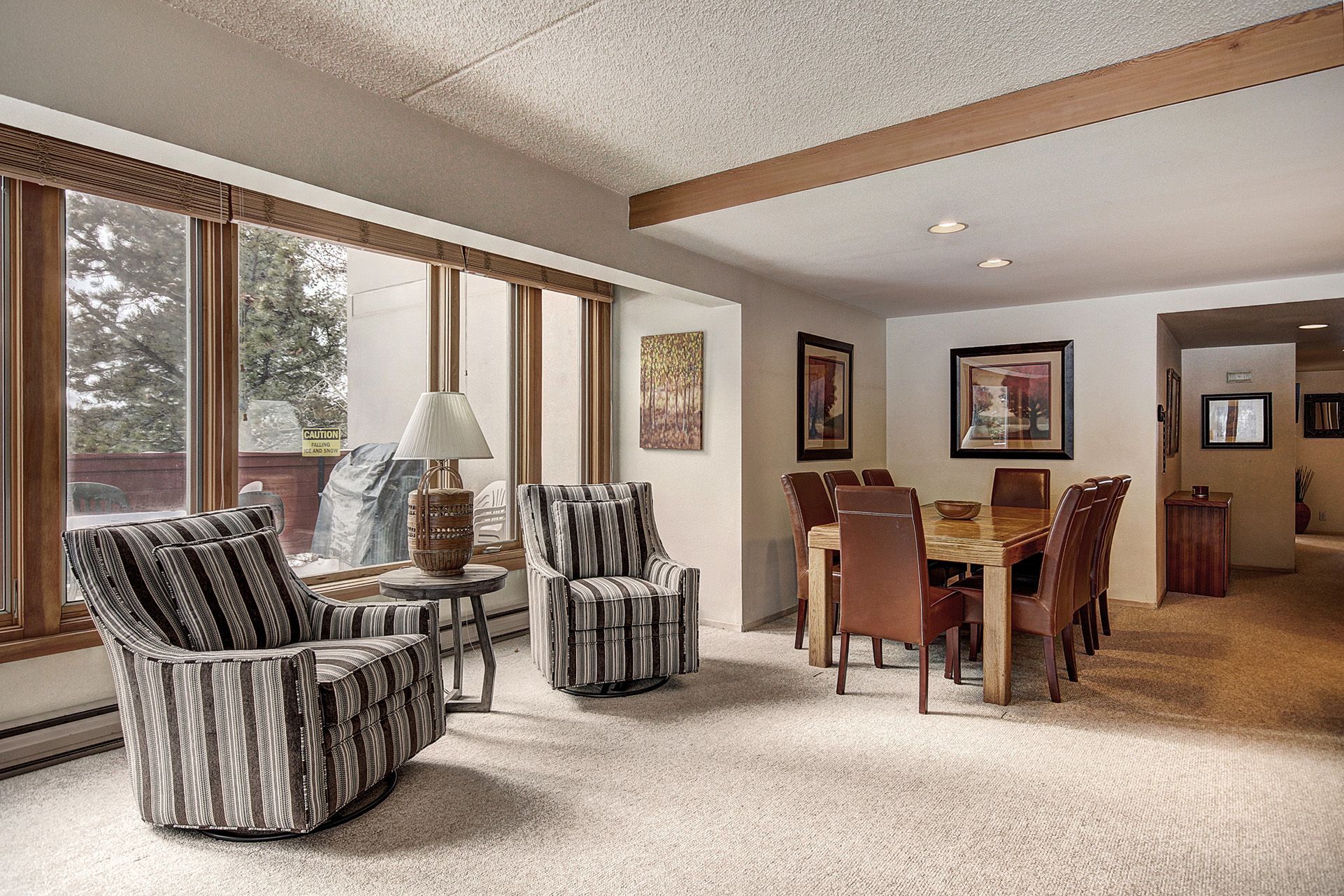A spacious living room with a large dining area, featuring striped armchairs, a wooden dining table, and a view through large windows.
