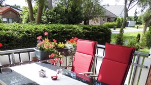 Un patio exterior con una mesa y sillas rojas, rodeado de follaje y un muro de ladrillo.