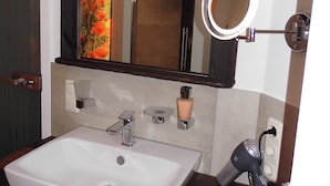 Un baño con un espejo grande, un lavabo, un perchero para toallas y una ducha.
