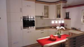 Una cocina moderna con armarios blancos, horno empotrado y una mesa roja con una cesta y una orquídea.
