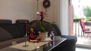 Una sala moderna con una mesa de comedor de vidrio, un sofá de color oscuro, una planta en maceta y un objeto decorativo rojo.