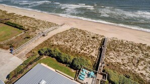 Vista aérea de una playa con una pasarela de madera que conduce a un edificio con piscina.