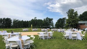 An outdoor event space with round tables covered in white tablecloths and white chairs, set up on a grassy lawn with trees in the background. - Large Home with Outstanding Views & Location (Palmer)