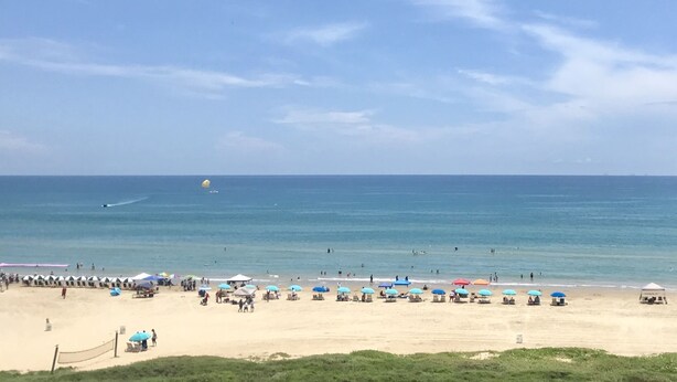 Une plage avec des parasols et des chaises longues, un ciel dégagé et un bateau au loin.