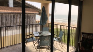 Un balcon avec une porte vitrée, une table, des chaises et une vue sur la plage.
