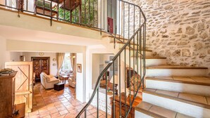 A spacious living area with a curved staircase, stone walls, and a view of greenery outside. - PROVENCE MAS IN A THOUSAND VINEYARDS VIEW ON MONT VENTOUX WITH POOL (Saint-Montan)