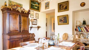 A dining area with a wooden table set for four, surrounded by chairs. A large wooden cabinet is to the left, and a bookshelf with books and decorative items is to the right. - PROVENCE MAS IN A THOUSAND VINEYARDS VIEW ON MONT VENTOUX WITH POOL (Saint-Montan)