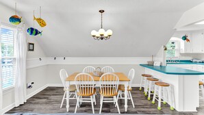 A dining area with a wooden table and white chairs, a kitchen with a blue countertop, and a ceiling with hanging fish decorations.