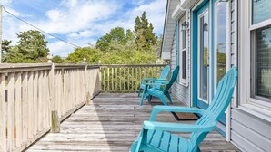 A wooden deck with two turquoise Adirondack chairs, a white railing, and a view of trees and a house with blue shutters.