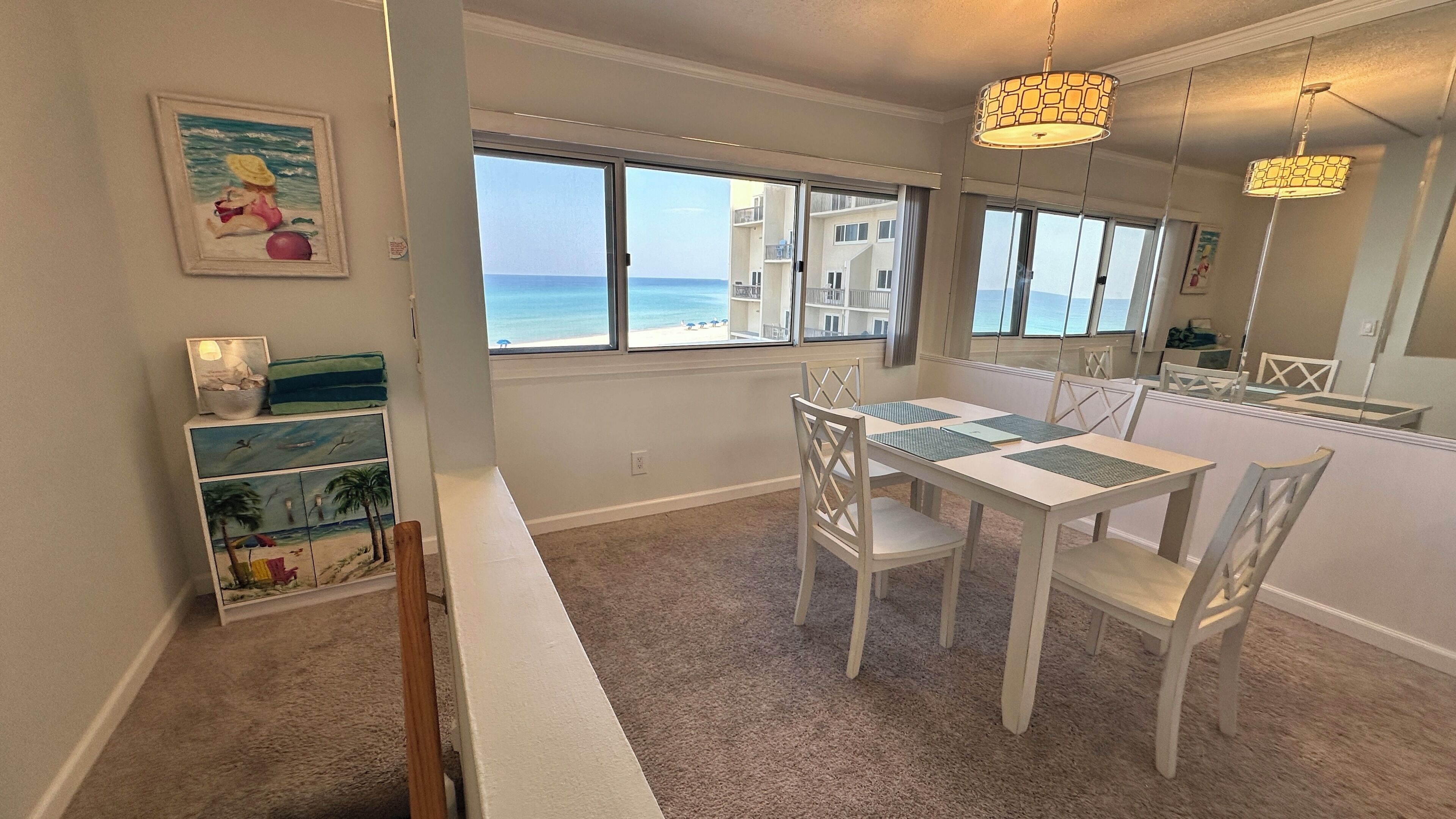 Uma sala de jantar com vista para o oceano, uma mesa branca com cadeiras e um lustre.