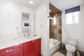 Een moderne badkamer met een wit wastafelmeubel, rode kastjes, een grote spiegel, een douche met glazen wanden en een wit toilet.