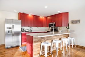 A modern kitchen with red cabinetry, a stainless steel refrigerator, a microwave, and a large island with bar stools.