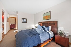 Een slaapkamer met een groot bed, een houten hoofdbord, een nachtkastje met een lamp en een schilderij aan de muur.