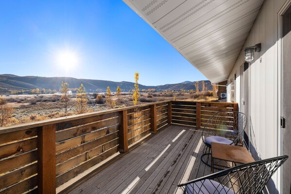 A wooden deck with a view of a dry, hilly landscape under a clear sky.