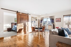 A spacious living area with a wooden floor, a dining table with chairs, a sofa, and a sliding barn door.