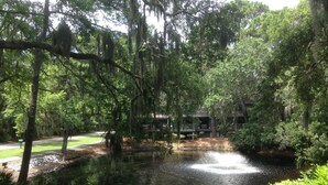 A pond surrounded by trees with hanging moss, a building with a porch, and a paved path. - Great Lagoon, Tennis+pool View Townhome W/10min Walk To Golf+Beach+Harbour Town (Hilton Head Island)