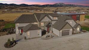 A large, two-story house with a garage, surrounded by a well-maintained lawn and a gravel driveway.