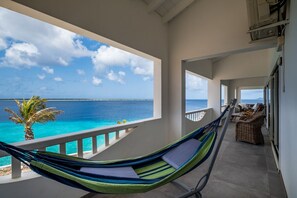 Un balcon avec un hamac, des meubles en osier et une vue sur l’océan.