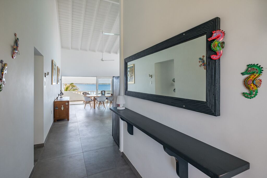 A hallway with a black console table, a large mirror with decorative seahorse ornaments, and a view of a dining area with chairs and a table.