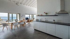 Eine moderne Küche mit einer großen Kochinsel, weißen Schränken und Blick auf das Meer.