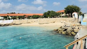 Klares, blaues Meer mit einem hölzernen Steg, der zu einem Sandstrand führt.