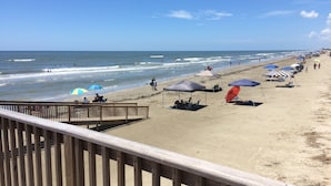 Ein Strand mit einer Holzpromenade, Strandstühlen und Menschen, die das Meer genießen.