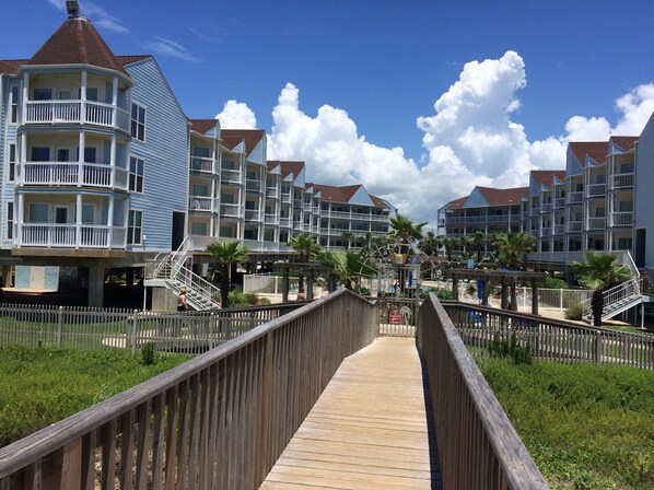 Une promenade en bois mène à un hôtel en bord de mer, doté de nombreux balcons et offrant une vue dégagée sur l’océan.