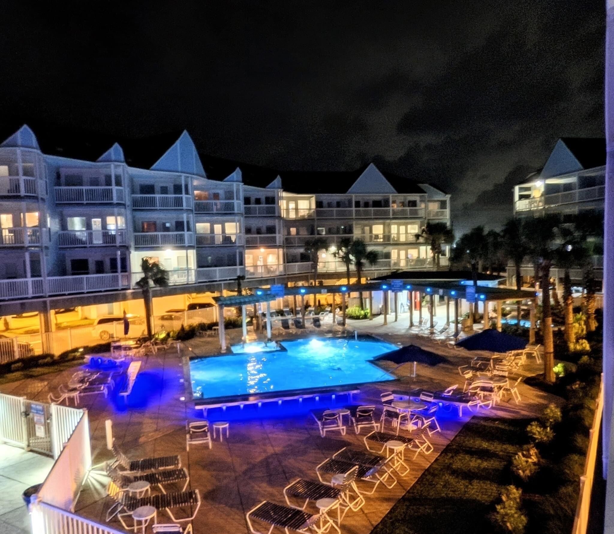 Et hotel med swimmingpool, liggestole og et godt oplyst udendørsområde om natten.
